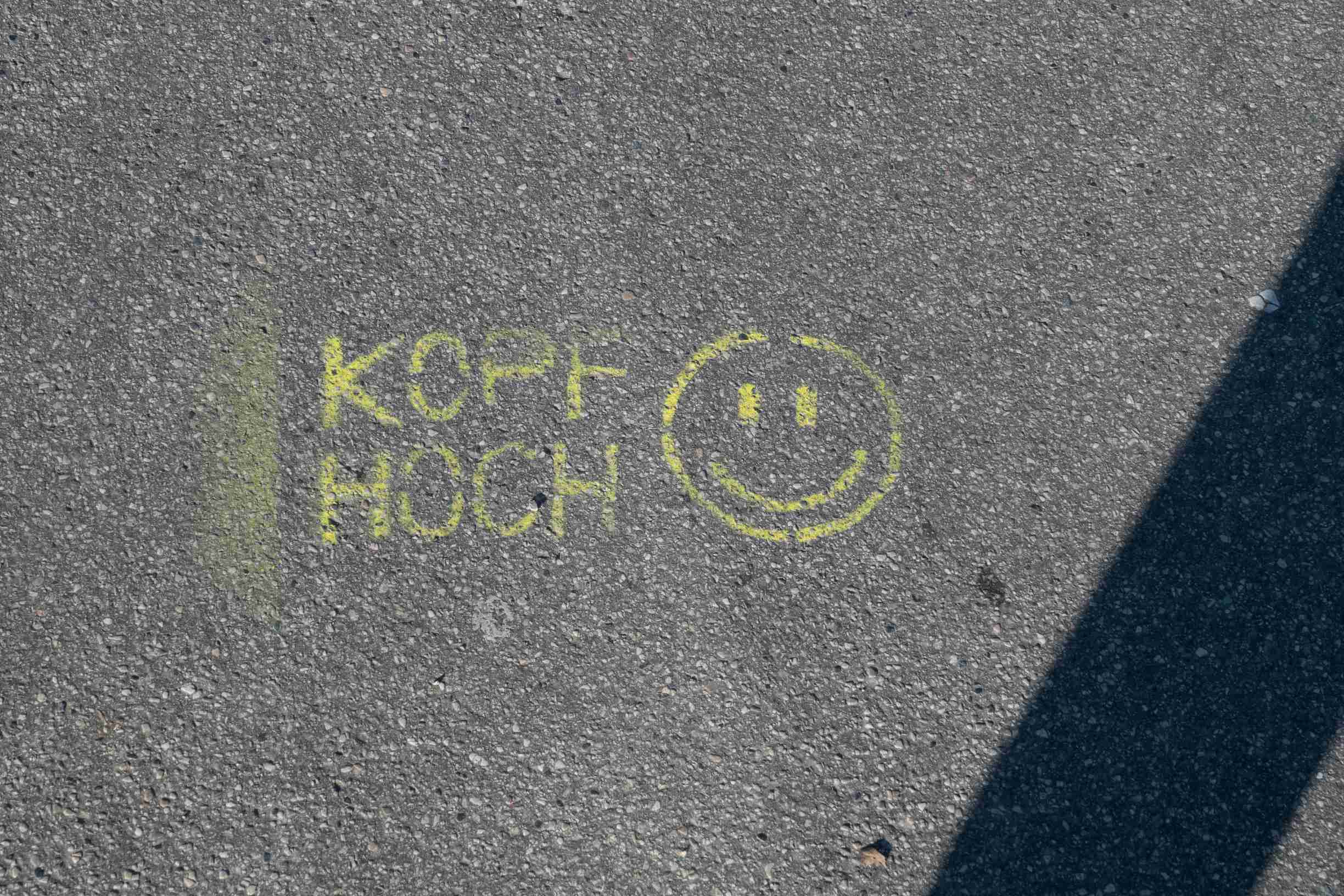 Marquage jaune au sol 'Souriez' en allemand (Kopf hoch)